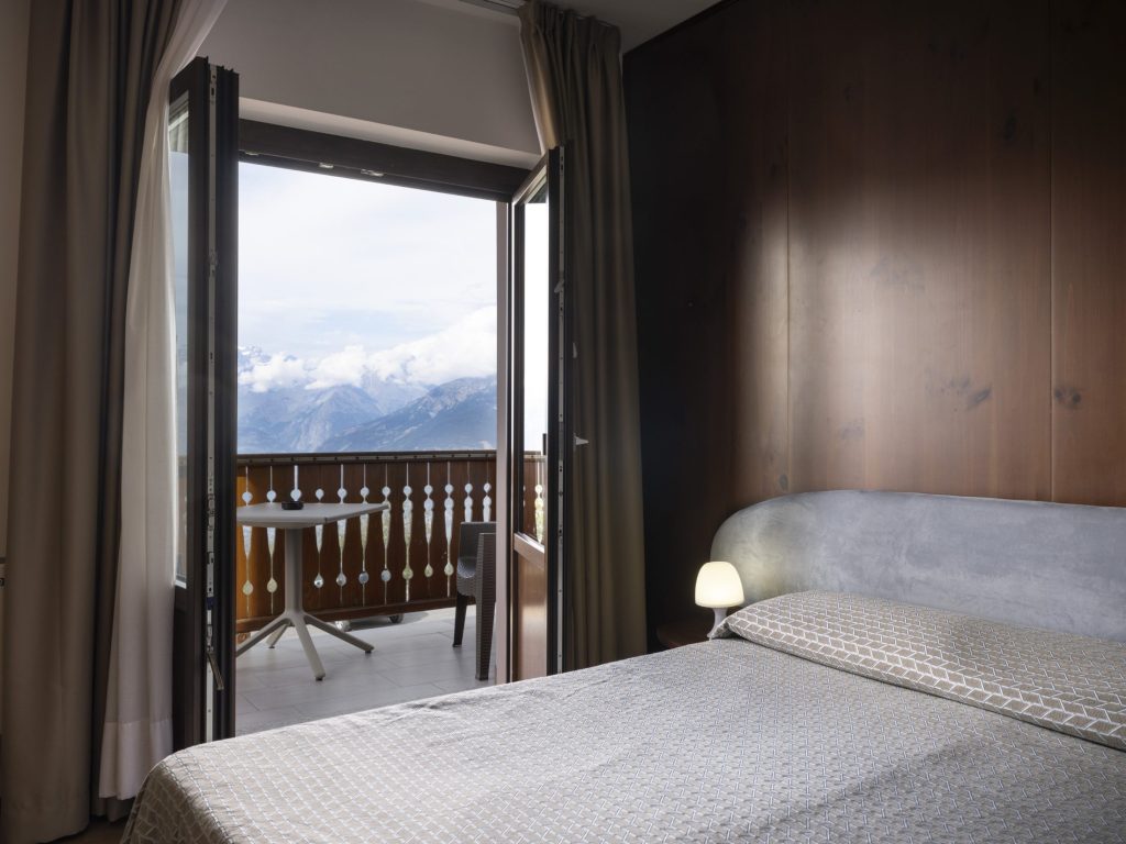 Camera con letto matrimoniale e balcone aperto sui prati di Pila