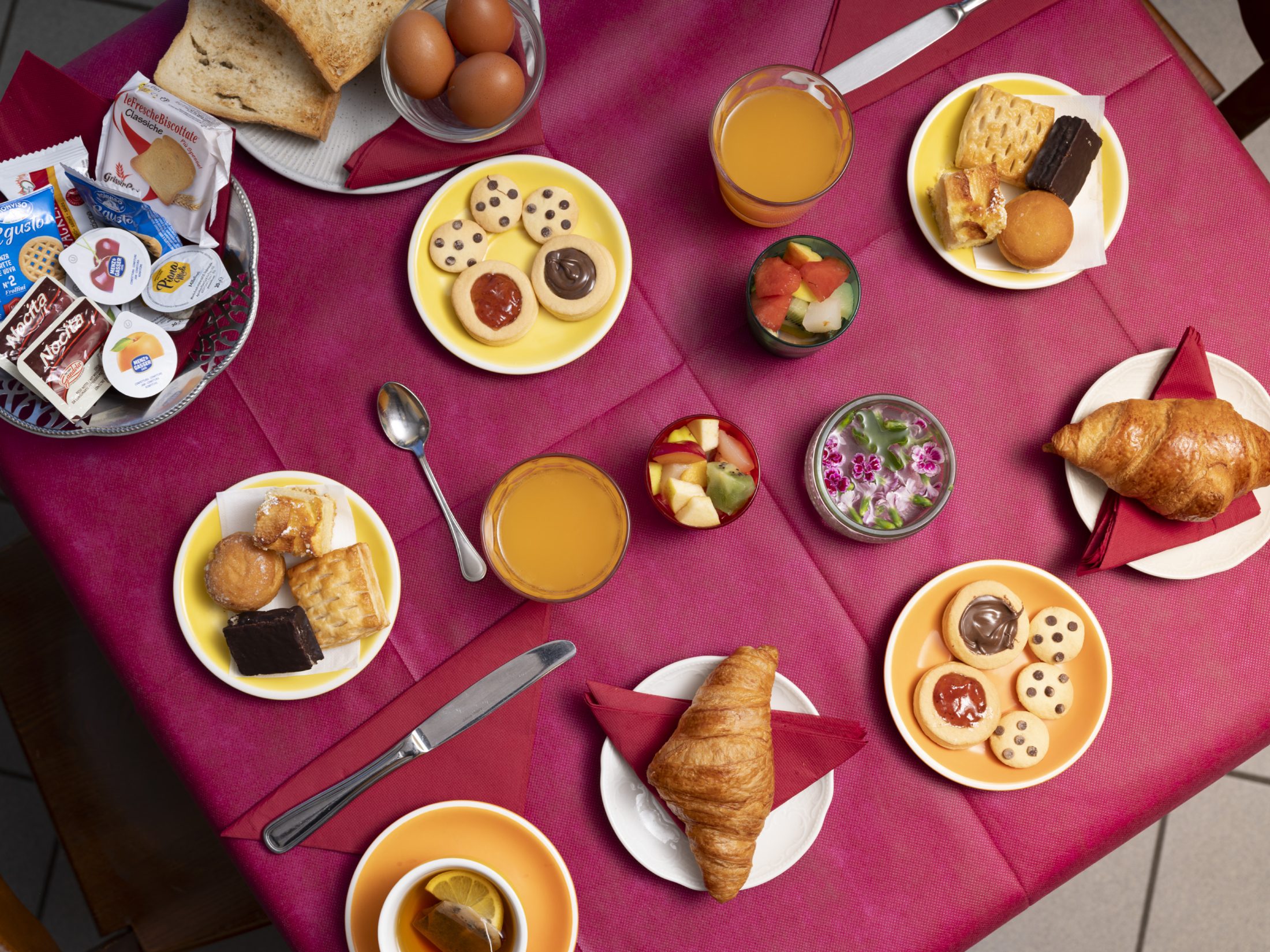 Tavola della colazione con croissant, biscotti, succo e frutta